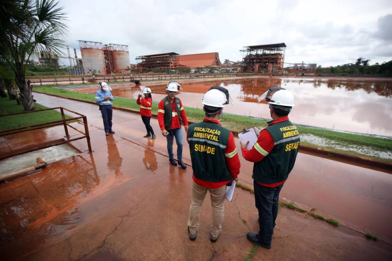 A Secretaria de Estado de Meio Ambiente e Sustentabilidade (Semas) notificou oficialmente a Hydro, na tarde desta terça-feira (27), por conta do não cumprimento do prazo de 48 horas dado pelo governo para que a empresa reduzisse os níveis das bacias de resíduos ao nível de, pelo menos, um metro, conforme determina a legislação ambiental. A notificação foi entregue por técnicos da Semas na sede da refinaria, em Barcarena, a 112 quilômetros de Belém. A determinação é que a produção de alumina seja reduzida pela metade. A Semas também triplicará a multa definida anteriormente, cumprindo a legislação ambiental em vigor, para R$ 1 milhão por dia de descumprimento (ou 300 mil Unidades de Padrão Fiscal). A empresa informou formalmente que reduziu os índices, mas não integralmente no total determinado de um metro. Técnicos das diretorias de Fiscalização e Licenciamento Ambiental da Semas acompanham diariamente o volume de água das bacias, tanto dos depósitos de rejeitos sólidos da indústria quanto do sistema de tratamento de água.
FOTO: THIAGO GOMES / AG PARÁ
DATA: 27.02.2018
BARCARENA - PARÁ <div class='credito_fotos'>Foto: Thiago Gomes /Ag. Pará | <a href='/midias/2018/originais/1d68418a-2563-4bd5-94b9-47d19e91c3a4.jpg' download><i class='fa-solid fa-download'></i> Download</a></div>