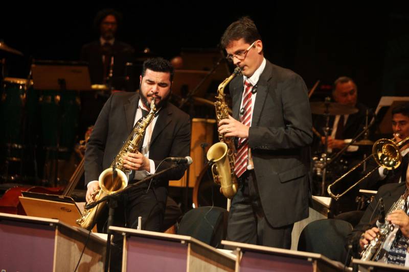 Os sons tradicionais de ritmos da Amazônia se misturaram com arranjos jazzísticos na noite de quinta-feira (15), no concerto “Celebrando o Theatro da Paz e Waldemar Henrique”, realizado pela Amazônia Jazz Band para comemorar os 140 anos do teatro e os 113 anos do maestro paraense, um dos mais importantes do país. Com a regência do maestro Nelson Neves, a noite teve uma convidada especial que encantou a plateia com seu tom de voz, a cantora Simone Almeida. O evento foi uma realização do Governo do Estado do Pará, por meio da Secretaria de Estado de Cultura (Secult) e da Academia Paraense de Música (APM). Para começar o espetáculo, “Foi Boto, Sinhá”, composição de Waldeco - como é carinhosamente chamado o regente e compositor - com arranjo de Tynnoko Costa, já arrebatou o público: sons de pássaros, barulhos de folhagens em movimento, de água. Um pouco da floresta era possível ouvir, de forma instrumental, em excelente execução dos músicos da big band. Logo depois, uma composição norte-americana deu o tom da noite de gala. Com sonoridade marcante, “The Phat Pack”, de Gordon Goodwin, mostrou como o jazz clássico pode combinar com a sonoridade da nossa região.
FOTO: CARLOS SODRÉ / AG PARÁ
DATA: 16.02.2018
BELÉM - PARÁ <div class='credito_fotos'>Foto: CARLOS SODRÉ / AG. PARÁ | <a href='/midias/2018/originais/212c6f5b-4309-42f8-be70-fd95b6f1f4e5.jpg' download><i class='fa-solid fa-download'></i> Download</a></div>