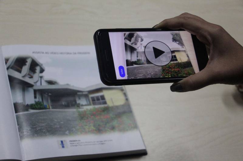 Se você achava que objetos pulando para fora da tela era coisa de filme de ficção científica, está na hora de rever seus conceitos. Aliás, o que acontece com a Realidade Aumentada (foto) é o contrário: você pula para dentro do mundo virtual para interagir com uma nova dimensão no modo como executamos tarefas. Essa tecnologia já está disponível no Prodepa RA, o software de Realidade Aumentada desenvolvido pela Empresa de Tecnologia da Informação e Comunicação do Estado do Pará (Prodepa). Hitoshi Seki, assessor da Prodepa, explica que Realidade Aumentada é uma tecnologia que permite que o mundo virtual seja misturado ao real, possibilitando maior interação. “O aplicativo lembra muito cenas do filme Harry Potter, quando mostrava um jornal e a imagem do jornal era animada, como se ela estivesse viva. O Prodepa RA faz isso também, só que através da tela do celular. Aponta-se o celular para uma imagem e essa imagem vai virar um vídeo, uma imagem em alta resolução ou até um áudio”.

FOTO: ASCOM / PRODEPA
DATA: 12.12.2018
BELÉM - PARÁ <div class='credito_fotos'>Foto: Ascom Prodepa   |   <a href='/midias/2018/originais/bc8f857b-8770-4e5f-9b70-35759824c772.jpg' download><i class='fa-solid fa-download'></i> Download</a></div>