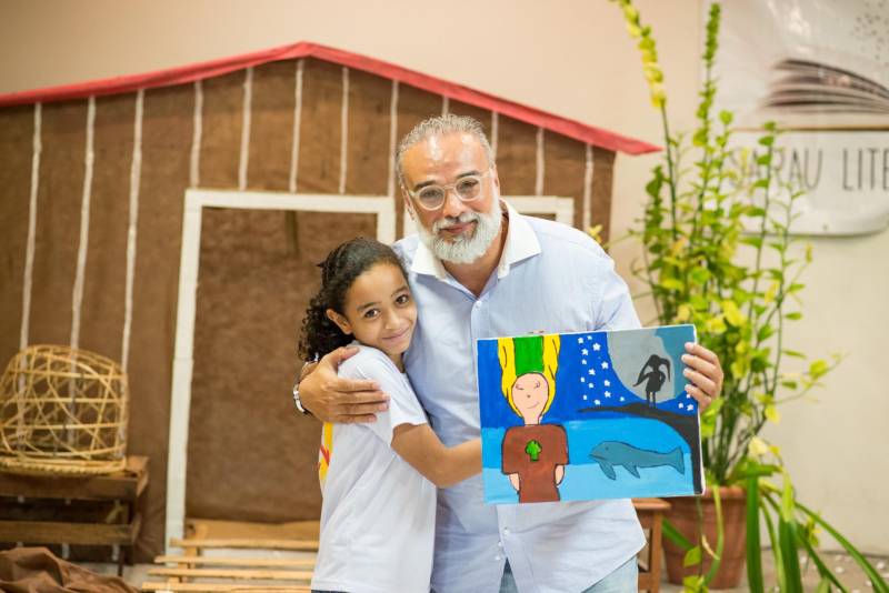 “A cultura tem o poder de emocionar”. A frase dita pela professora Ruth Valin marcou o tom do Sarau Literário na manhã desta sexta-feira, 8, no Preventório Santa Terezinha, no bairro do Marco, em Belém, que contou com a presença do escritor paraense Daniel Leite (com barba), homenageado pelas crianças atendidas pela instituição e os alunos da Escola Estadual Santa Terezinha, que funciona no mesmo prédio. Elas cantaram músicas infantis e recitaram trechos das obras “A história das crianças que plantaram um rio” e “A menina árvore”, de Daniel Leite, além de apresentar uma dramatização sobre a primeira obra. Muito concentrados e com a leitura bem ensaiada, os pequeninos emocionaram a todos, principalmente o escritor convidado para o sarau. Segundo a professora Odinéia Bastos, que orientou os alunos na leitura do livro “A história das crianças que plantaram um rio”, elas soltaram a imaginação durante a leitura da obra, e dessa viagem saíram desenhos, pinturas, colagens e poemas, que enfeitaram o auditório e os corredores da instituição, encantando a todos os presentes.
FOTO: FERNANDO SETTE CÂMARA / ASCOM IOE
DATA: 08.06.2018
BELÉM - PARÁ <div class='credito_fotos'>Foto: FERNANDO SETTE CÂMARA / ASCOM IOE | <a href='/midias/2018/originais/d3f453ad-4108-4f92-8d1d-541449532908.jpg' download><i class='fa-solid fa-download'></i> Download</a></div>