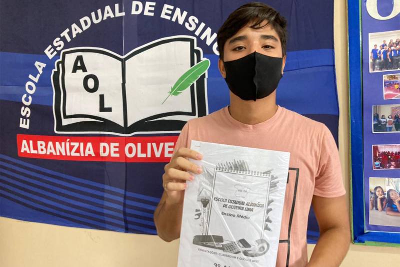 O aluno da 3ª série do médio, Kevin, recebndo o cadenos de atividade.