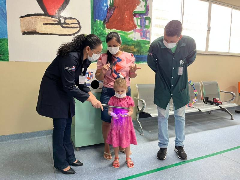 Com o uso de uma luz especial e de uma substância fluorescente, crianças acompanhavam a simulação da presença de microorganismos nas mãos