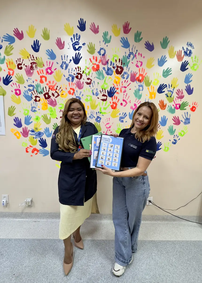 atacha Cardoso, coordenadora de Humanização do Hoiol, e Elizabeth Cabeça, assistente do Escritório de Experiência do Paciente do Hoiol, posam com os cadernos "Memórias da Cura”. 